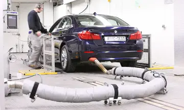 Blauer BMW auf einem Prüfstand für Abgastests. Ein Techniker überwacht die Messungen, die für die Euro 6-Abgasnorm relevant sind.