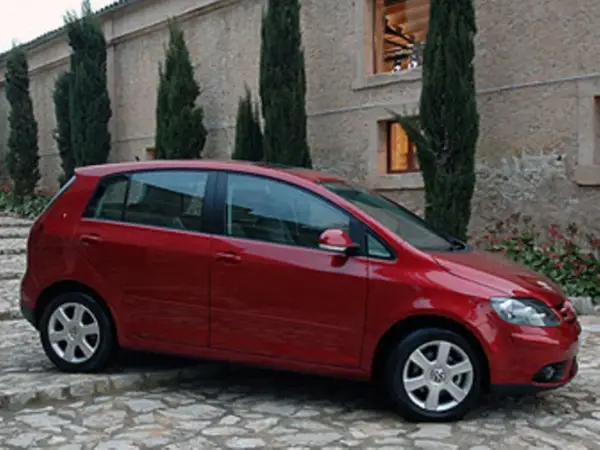 Roter VW Golf Plus mit Automatikgetriebe, der vor einem Steingebäude parkt. Mögliche Probleme mit dem Automatikgetriebe sind ein Thema.
