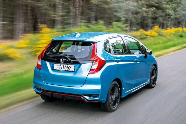 Blauer Honda Jazz Hybrid fährt auf einer Landstraße. Trotz der schönen Fahrt gibt es Berichte über Honda Jazz Hybrid Probleme.