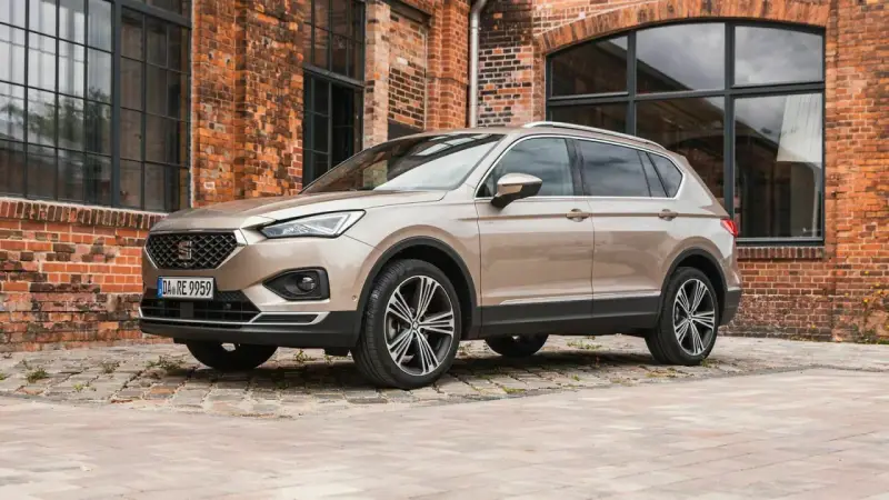 Beiger Seat Tarraco vor Backsteinhaus. Keine Seat Tarraco Probleme hier, nur stilvolles Fahren.