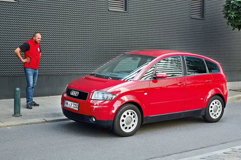 Mann steht neben rotem Audi A2, der für seine audi a2 schwachstellen bekannt ist.
